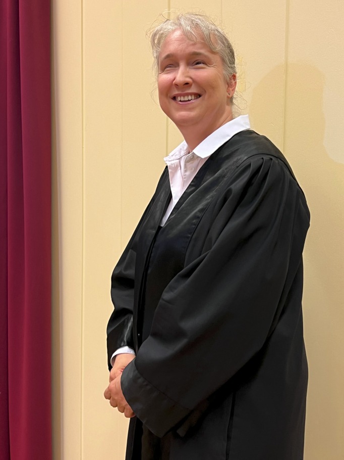 Pamela Pabst stehend, in Robe,nach links gewandt, Blick in Richtung Kamera, vor weißen Paneelen mit weinrotem Vorhangsaum am linken Rand